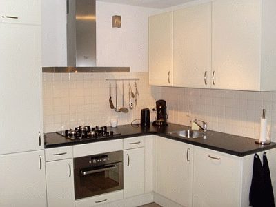 Geplaatste keuken met witte fronten, zwart werkblad en betegelde achterwand.