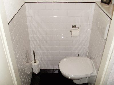 Gerenoveerd toilet met witte metrotegels, een zwarte vloer en een hangend toilet.